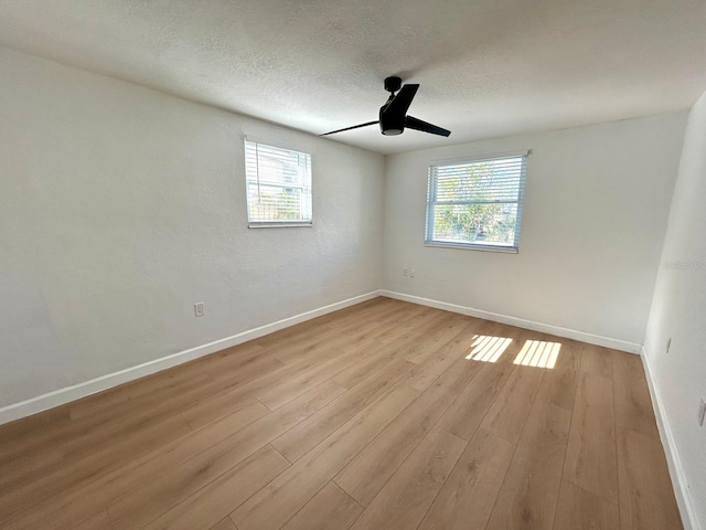 unfurnished room with a textured ceiling, ceiling fan, light wood-type flooring, and a wealth of natural light