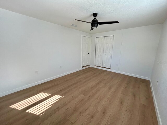 unfurnished bedroom featuring a closet, a textured ceiling, baseboards, and wood finished floors