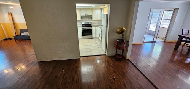 kitchen with stainless steel range, backsplash, freestanding refrigerator, white cabinetry, and hardwood / wood-style floors