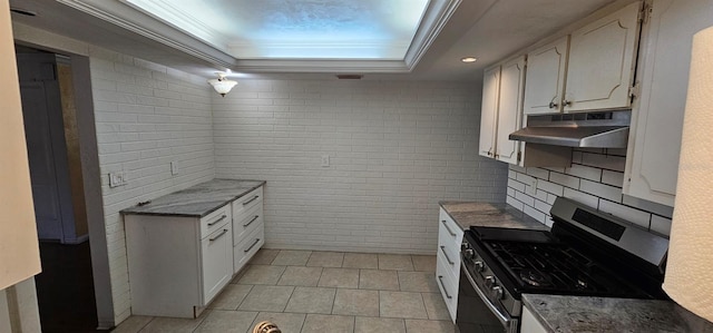 kitchen with under cabinet range hood, white cabinets, ornamental molding, stainless steel gas range, and a raised ceiling