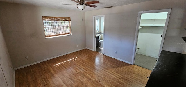 unfurnished bedroom featuring a walk in closet, a closet, ensuite bathroom, wood finished floors, and baseboards