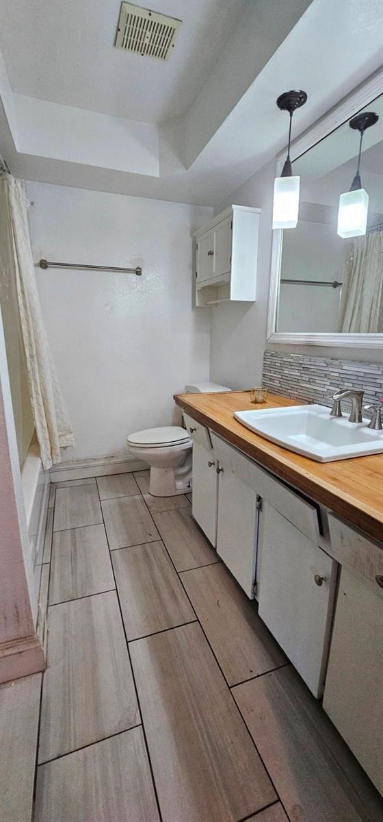 full bathroom featuring toilet, vanity, visible vents, and decorative backsplash