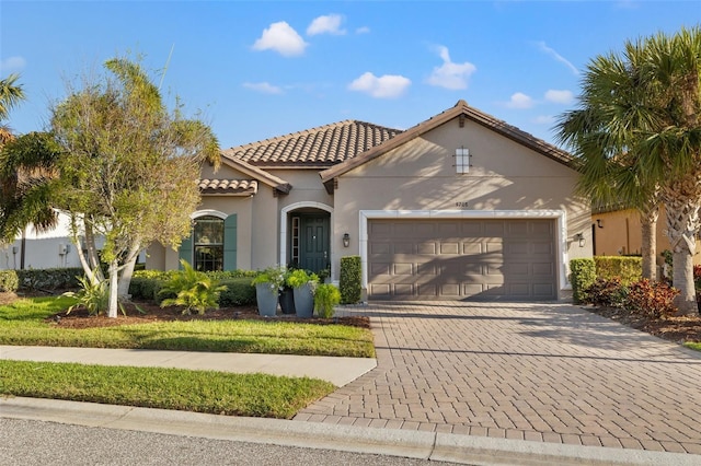 mediterranean / spanish home featuring stucco siding, an attached garage, a tile roof, and decorative driveway