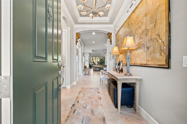 foyer featuring a raised ceiling, arched walkways, an inviting chandelier, crown molding, and baseboards