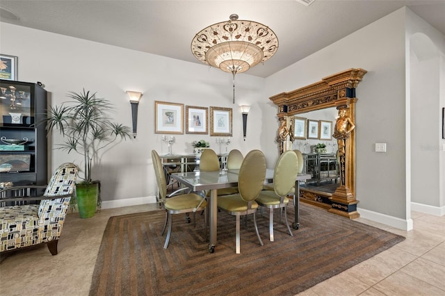 dining space featuring tile patterned floors, arched walkways, and baseboards