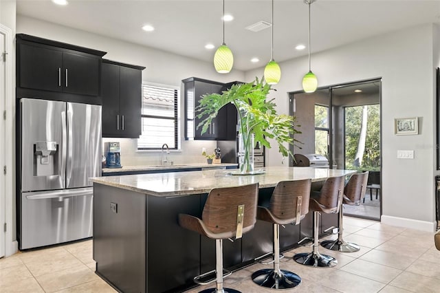 kitchen featuring visible vents, a sink, stainless steel fridge, dark cabinets, and a center island