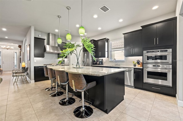 kitchen featuring visible vents, wall chimney range hood, dark cabinets, stainless steel appliances, and a sink