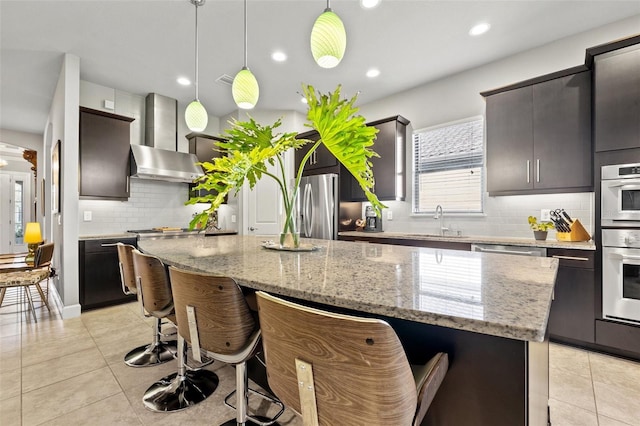 kitchen featuring light tile patterned flooring, freestanding refrigerator, pendant lighting, a kitchen bar, and wall chimney range hood