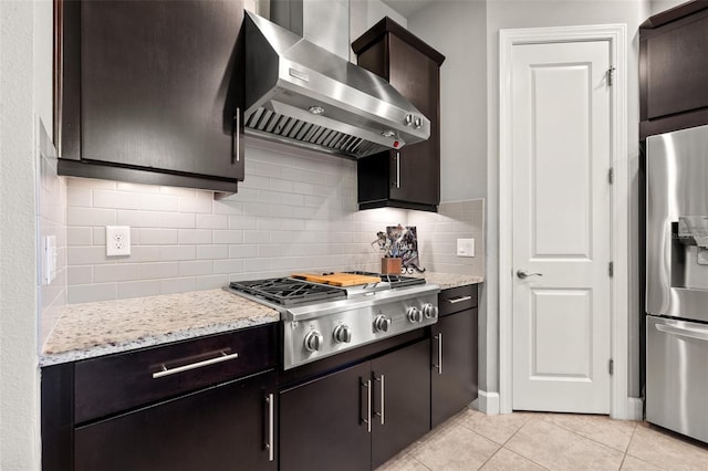 kitchen featuring light tile patterned floors, light stone countertops, appliances with stainless steel finishes, wall chimney range hood, and backsplash