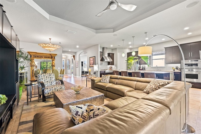 living area featuring recessed lighting, arched walkways, a textured ceiling, a raised ceiling, and a ceiling fan