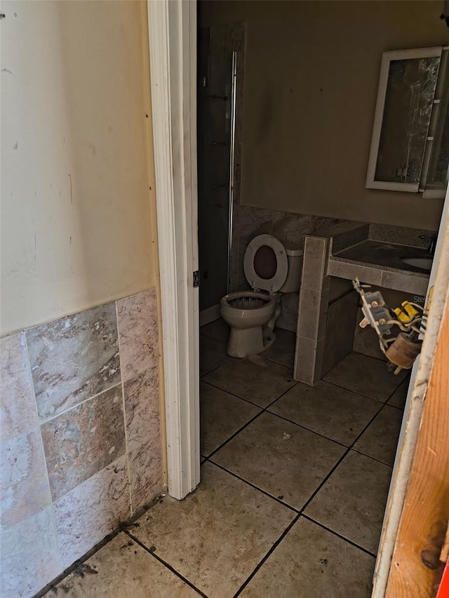 bathroom with toilet, wainscoting, tile walls, and tile patterned floors