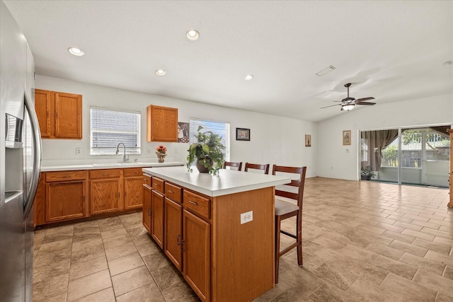 kitchen featuring stainless steel fridge, a kitchen bar, brown cabinetry, and a center island