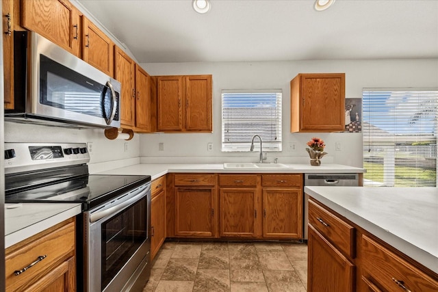 kitchen featuring brown cabinetry, stainless steel appliances, light countertops, a sink, and recessed lighting