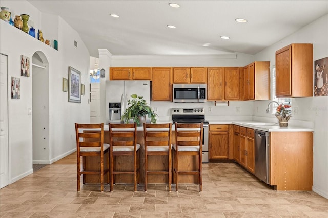 kitchen with a sink, a center island, light countertops, appliances with stainless steel finishes, and brown cabinets