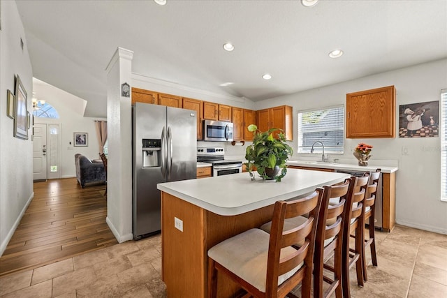 kitchen featuring a kitchen island, appliances with stainless steel finishes, brown cabinets, light countertops, and a sink