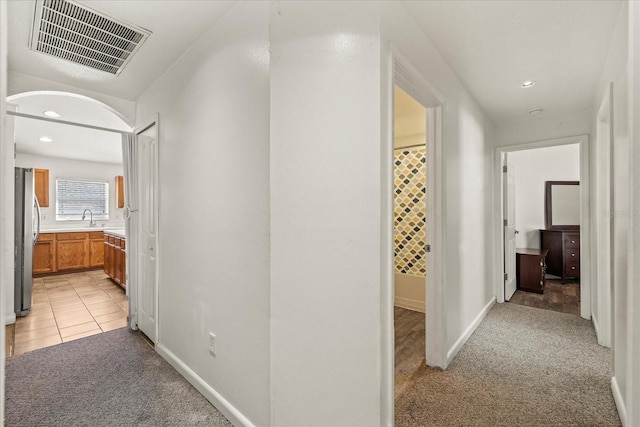 corridor featuring light carpet, visible vents, a sink, and recessed lighting