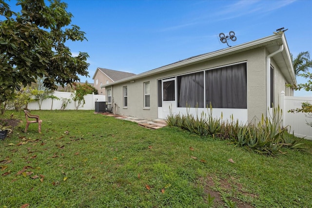 back of property with central air condition unit, fence private yard, a lawn, and stucco siding