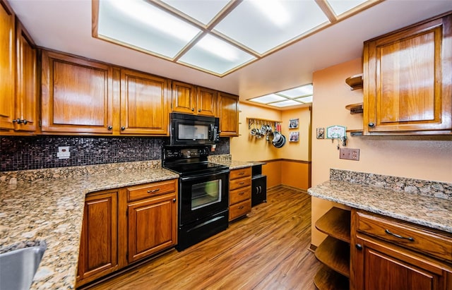 kitchen with open shelves, brown cabinetry, built in study area, light wood-type flooring, and black appliances