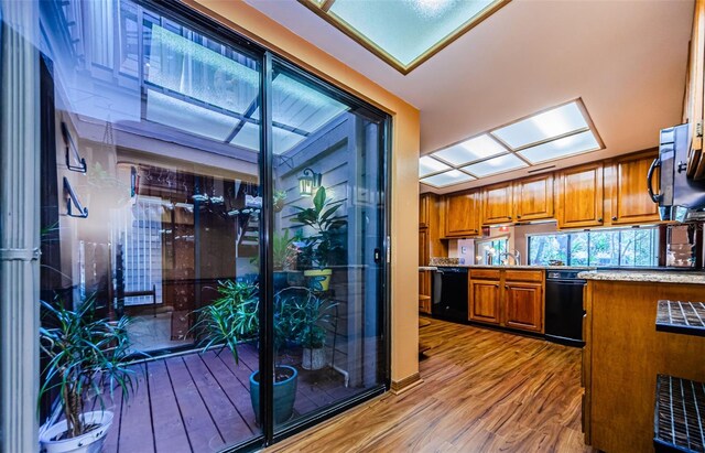 kitchen with a skylight, brown cabinets, a sink, wood finished floors, and black appliances