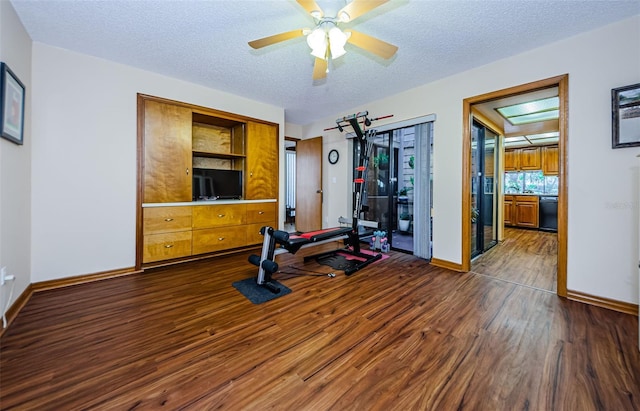 exercise area featuring dark wood-style flooring, ceiling fan, a textured ceiling, and baseboards