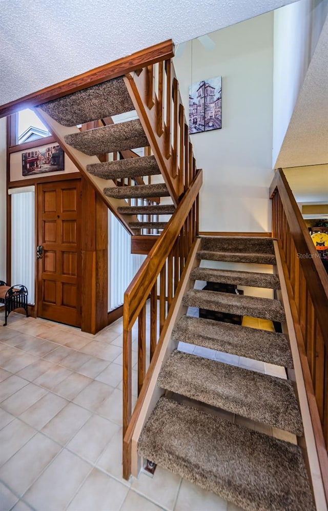 stairway with a textured ceiling, baseboards, and tile patterned floors