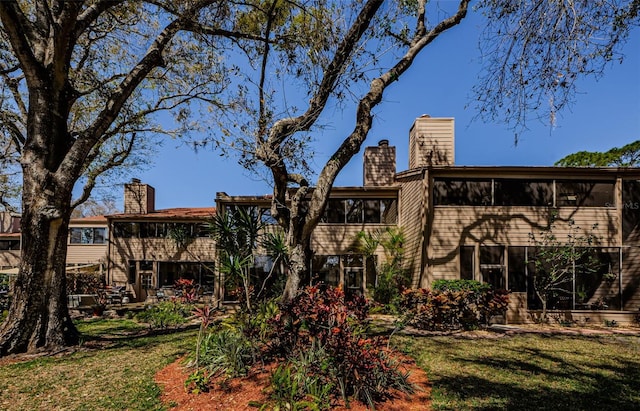 back of property featuring a lawn, a chimney, and a sunroom