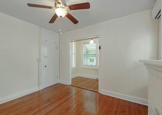 empty room featuring ceiling fan, a wall unit AC, wood finished floors, and baseboards