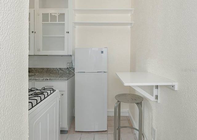 kitchen with light tile patterned floors, glass insert cabinets, freestanding refrigerator, decorative backsplash, and gas range