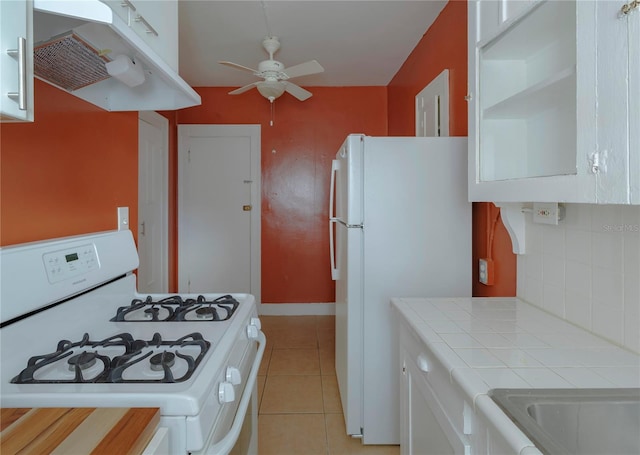 kitchen featuring under cabinet range hood, white appliances, white cabinetry, tile counters, and decorative backsplash