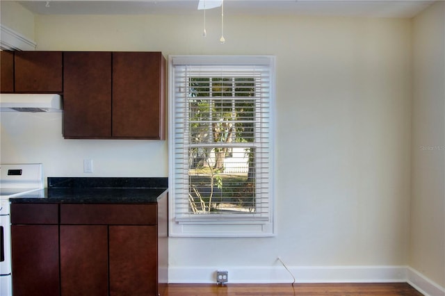 kitchen with white range with electric stovetop, dark stone counters, under cabinet range hood, and baseboards