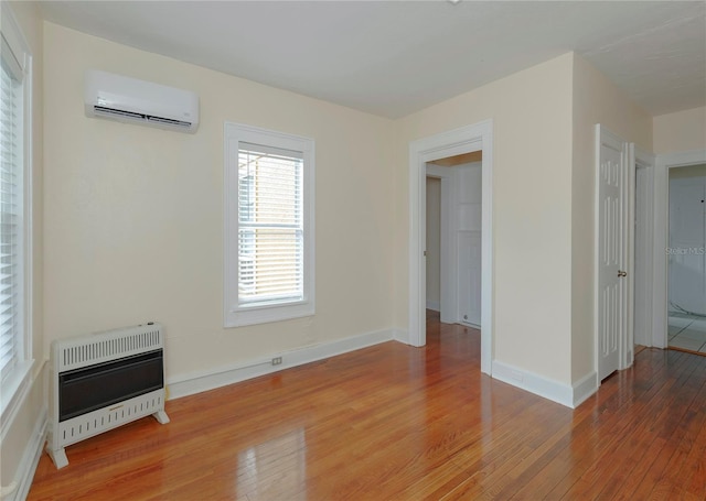 interior space featuring heating unit, light wood finished floors, baseboards, and a wall mounted AC
