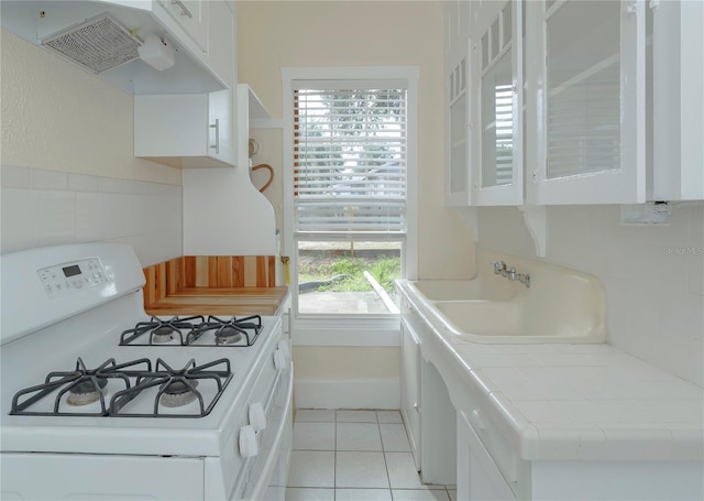 kitchen with light tile patterned floors, tile counters, white cabinetry, white range with gas cooktop, and under cabinet range hood