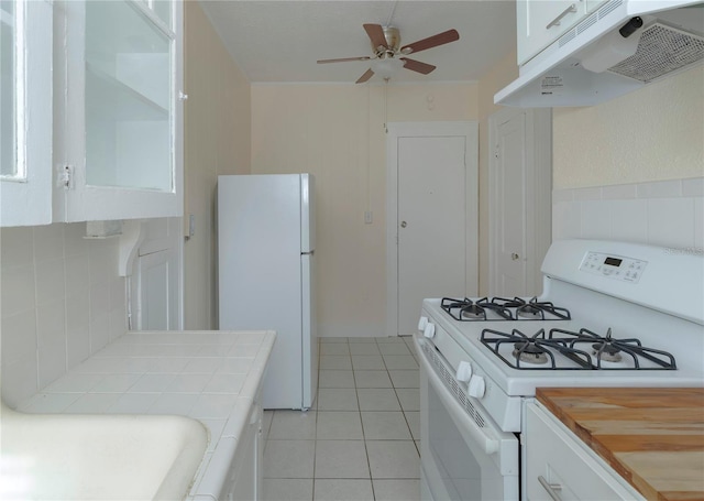 kitchen with light tile patterned flooring, under cabinet range hood, white appliances, white cabinetry, and tile counters