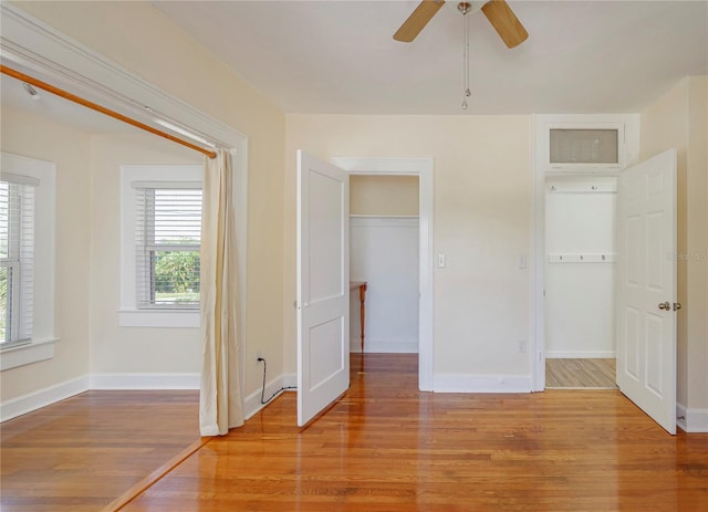 unfurnished bedroom with light wood-type flooring, ceiling fan, a spacious closet, and baseboards