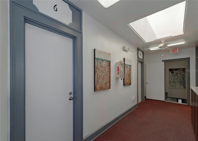 hall featuring a skylight, dark carpet, and baseboards