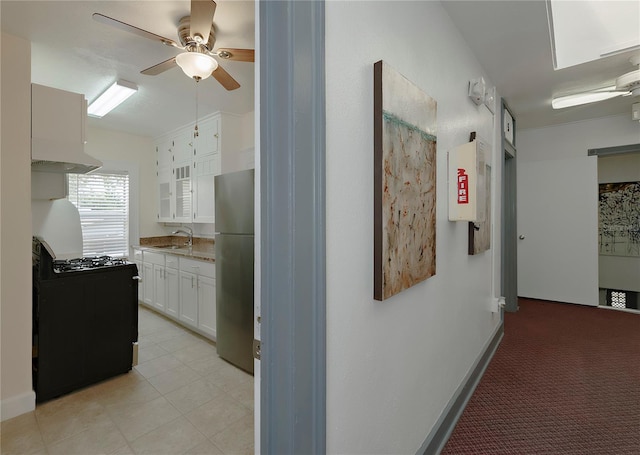 kitchen with a sink, a ceiling fan, white cabinetry, freestanding refrigerator, and gas range
