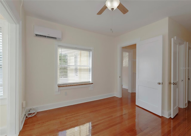 empty room featuring light wood-style floors, ceiling fan, baseboards, and a wall mounted AC