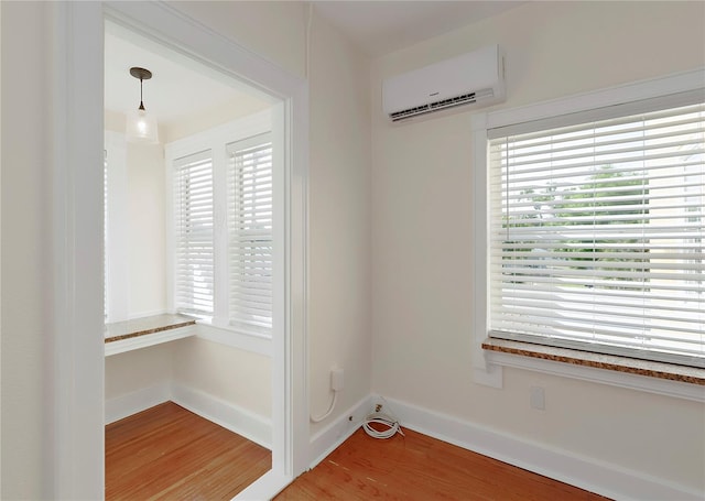 interior space with light wood-type flooring, a wall unit AC, and baseboards