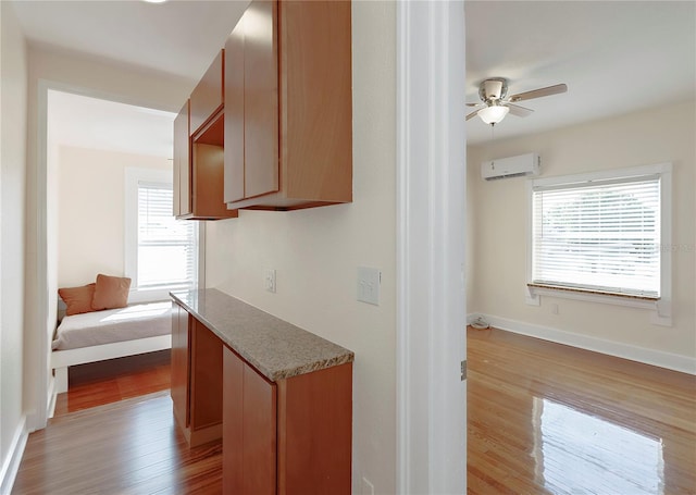 kitchen featuring ceiling fan, a wall unit AC, wood finished floors, and baseboards