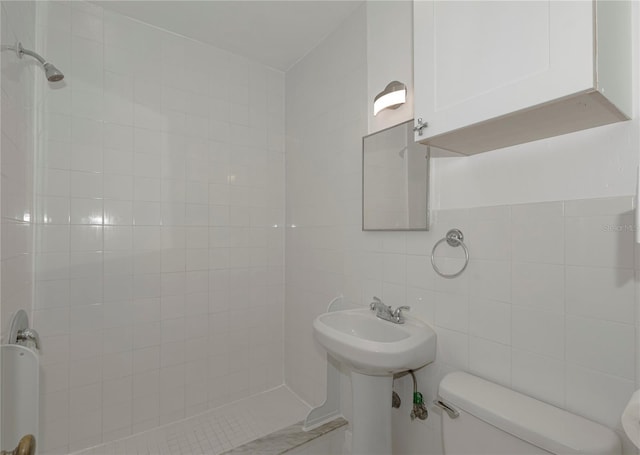 bathroom with a tile shower, toilet, and tile walls