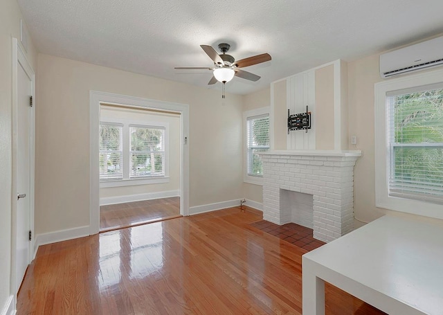 unfurnished living room featuring light wood-style floors, a brick fireplace, an AC wall unit, and plenty of natural light