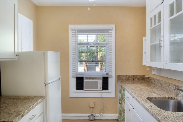 kitchen with freestanding refrigerator, white cabinets, a sink, light stone countertops, and cooling unit