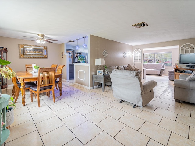 living room featuring light tile patterned floors, visible vents, baseboards, and a ceiling fan