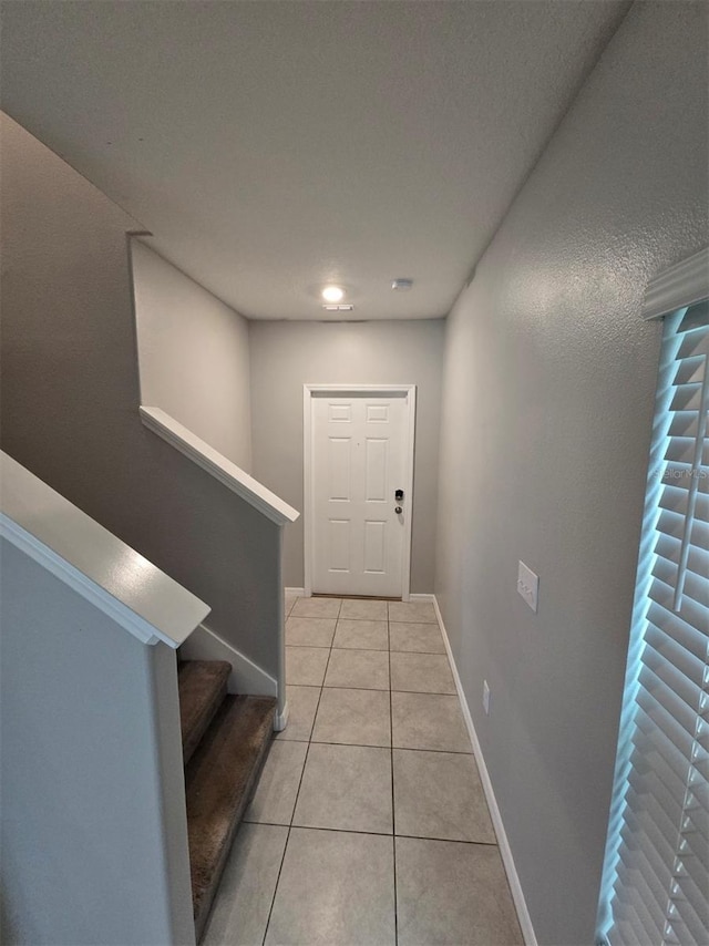 corridor featuring stairway, light tile patterned flooring, and baseboards