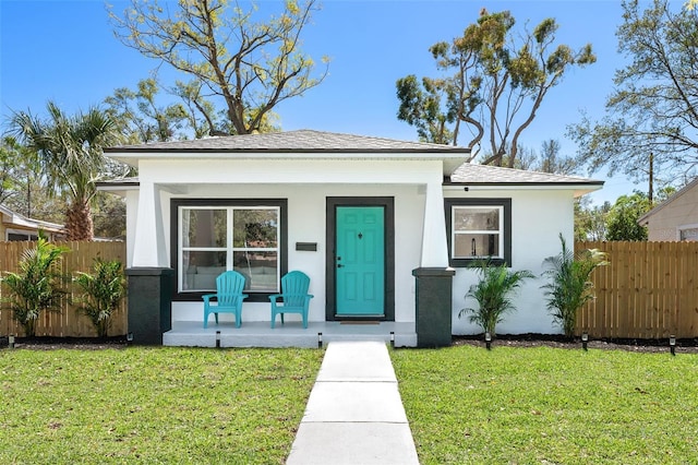 bungalow with covered porch, fence, and a front lawn