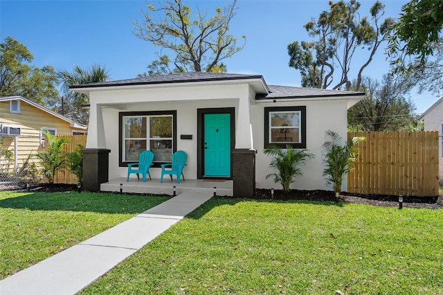 bungalow-style house featuring a front yard, fence, a porch, and stucco siding