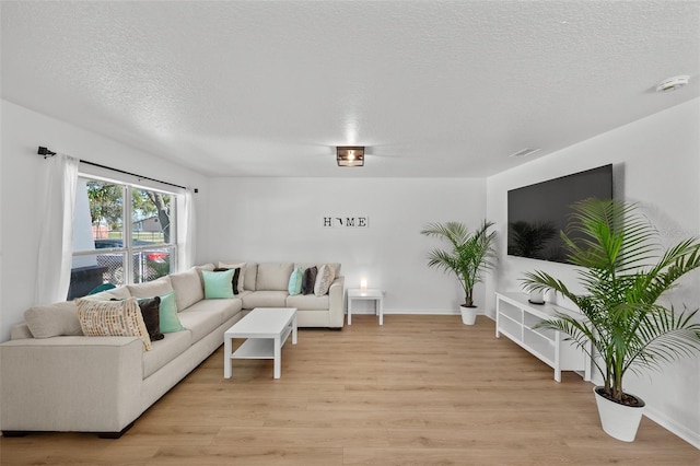 living room with a textured ceiling, light wood-type flooring, visible vents, and baseboards