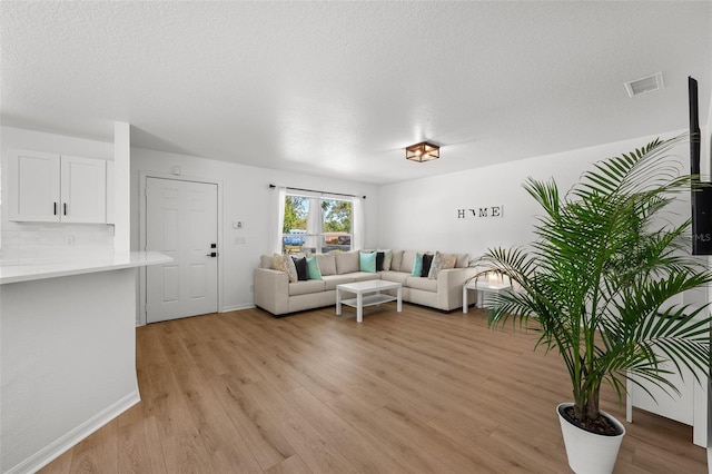 living room featuring light wood finished floors, baseboards, visible vents, and a textured ceiling