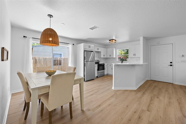 dining room with light wood-type flooring, visible vents, and a textured ceiling