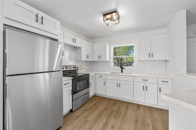 kitchen featuring light wood finished floors, white cabinets, appliances with stainless steel finishes, light countertops, and a sink